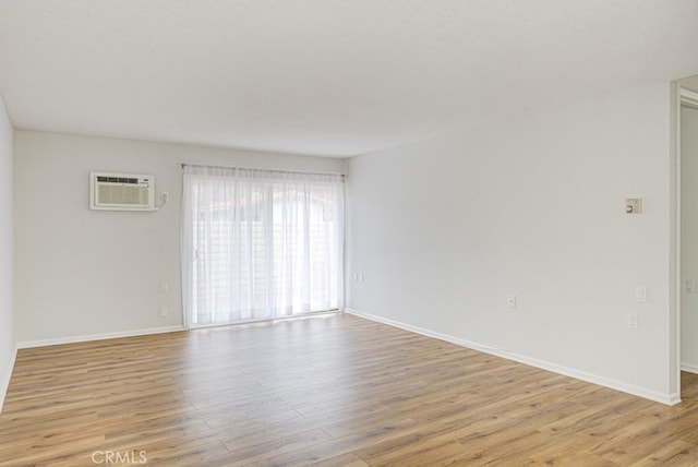 spare room featuring an AC wall unit, baseboards, and light wood-style floors