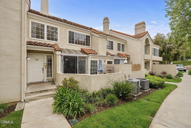 view of front of house with fence, stucco siding, a chimney, central AC unit, and a tiled roof