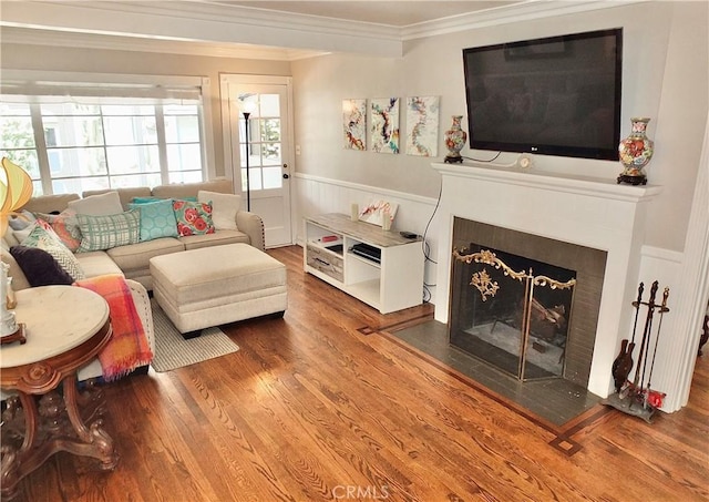 living room with a fireplace with flush hearth, ornamental molding, wood finished floors, and a wainscoted wall