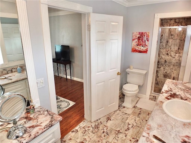 bathroom with a shower stall, vanity, baseboards, toilet, and ornamental molding