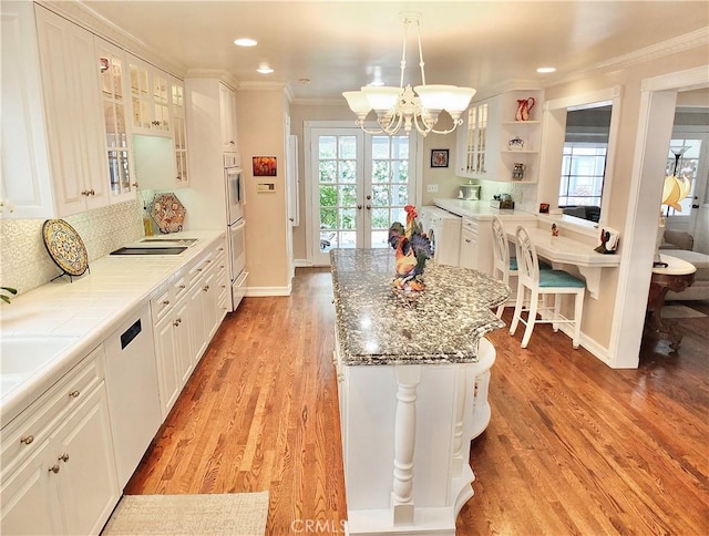 kitchen featuring crown molding, light wood finished floors, a chandelier, baseboards, and decorative backsplash