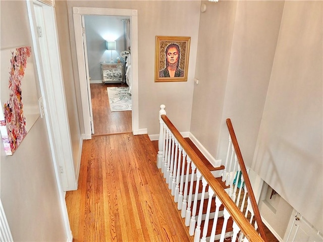 hallway with baseboards, light wood finished floors, and an upstairs landing