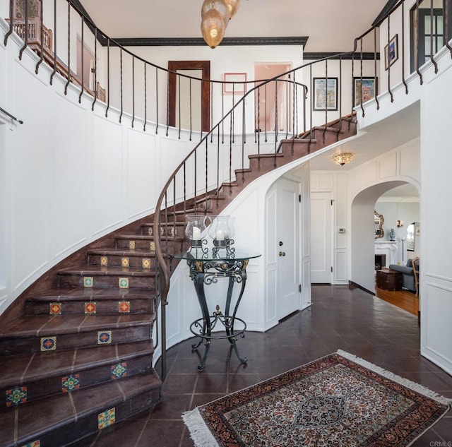 entrance foyer featuring crown molding, arched walkways, stairway, and a towering ceiling