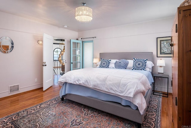 bedroom with baseboards, a chandelier, wood finished floors, and visible vents