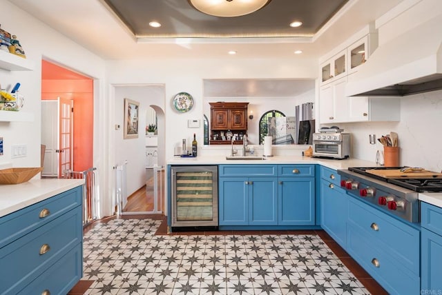 kitchen featuring wine cooler, stainless steel gas stovetop, custom range hood, a sink, and blue cabinetry