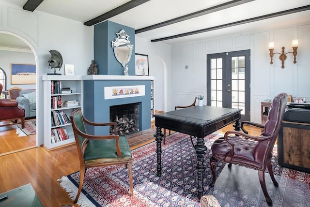 interior space with a decorative wall, a fireplace, french doors, wood finished floors, and beamed ceiling