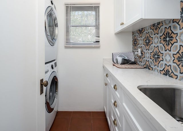 clothes washing area with cabinet space, dark tile patterned floors, a sink, and stacked washer and clothes dryer