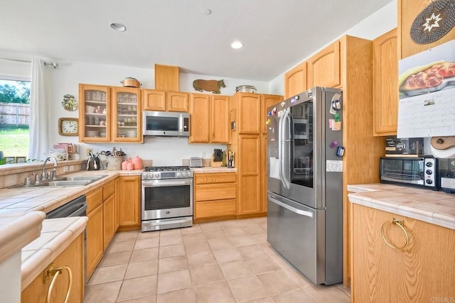 kitchen featuring tile countertops, a sink, appliances with stainless steel finishes, and glass insert cabinets