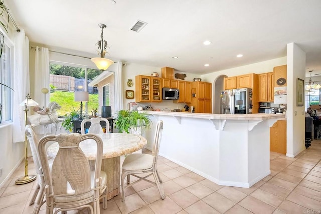 kitchen with a breakfast bar area, stainless steel appliances, a peninsula, visible vents, and glass insert cabinets