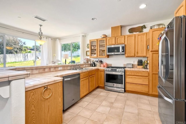 kitchen with a sink, tile counters, stainless steel appliances, visible vents, and glass insert cabinets