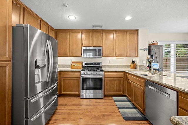 1752 Cottonwood Dr, Vista, CA 92081 - kitchen featuring appliances with stainless steel finishes, a sink, light wood-type flooring, brown cabinets, and light stone counters