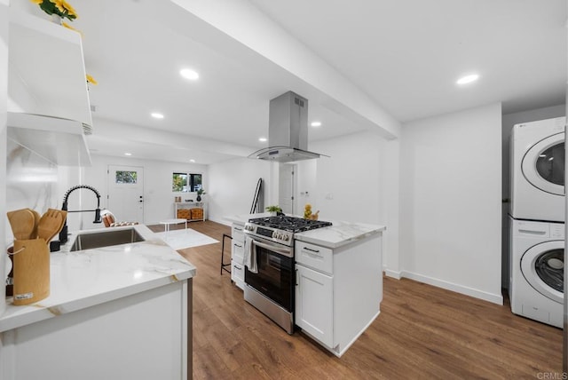 kitchen with island range hood, white cabinetry, stainless steel range with gas stovetop, a sink, and stacked washer / drying machine