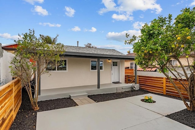 view of front of property featuring fence private yard, a shingled roof, stucco siding, and a patio