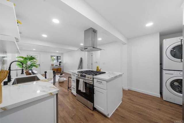 kitchen featuring a sink, stainless steel gas stove, stacked washer / dryer, wood finished floors, and island range hood