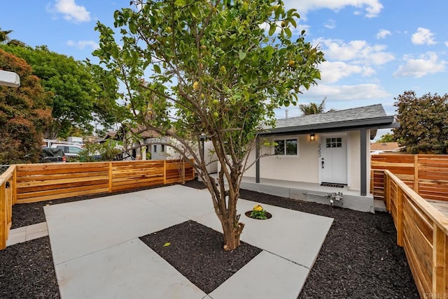 view of front of property featuring a shingled roof, a fenced backyard, and a patio area
