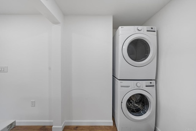 laundry area with laundry area, baseboards, wood finished floors, and stacked washer / dryer