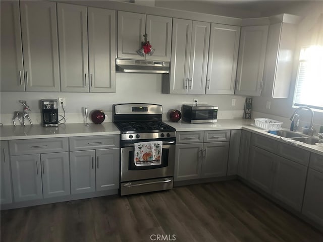 kitchen featuring appliances with stainless steel finishes, a sink, light countertops, under cabinet range hood, and gray cabinetry