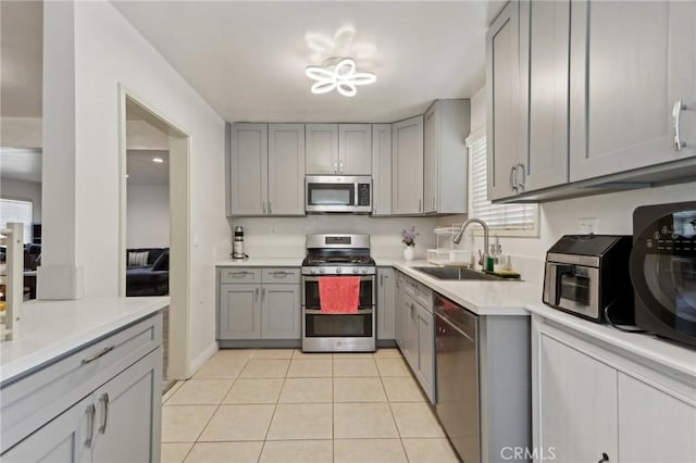 kitchen featuring light countertops, a sink, light tile patterned floors, gray cabinetry, and stainless steel appliances