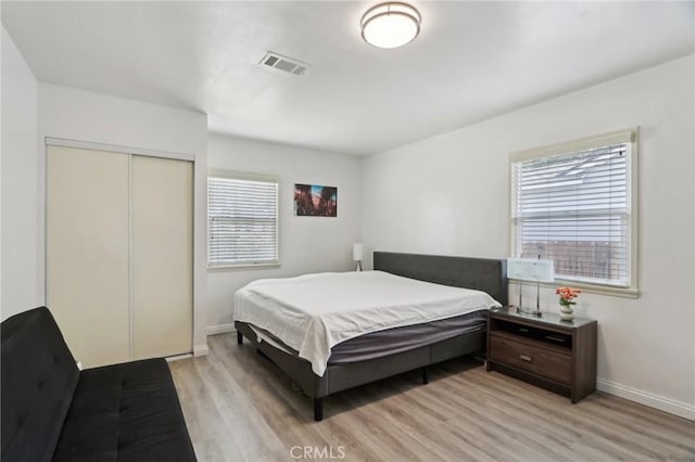 bedroom with visible vents, light wood finished floors, baseboards, and a closet
