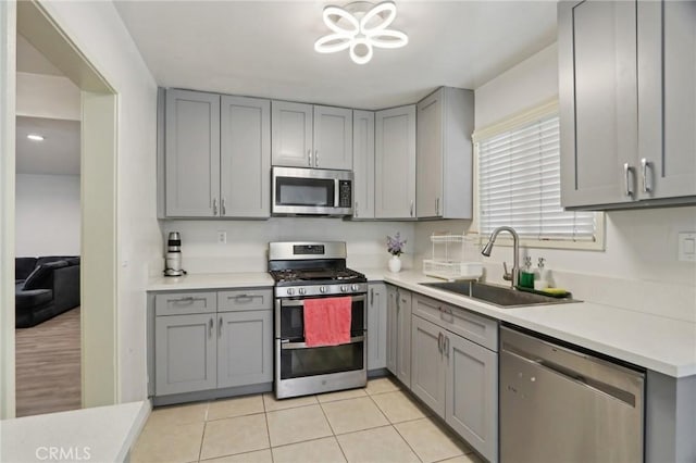 kitchen with gray cabinets, appliances with stainless steel finishes, a sink, light tile patterned floors, and light countertops