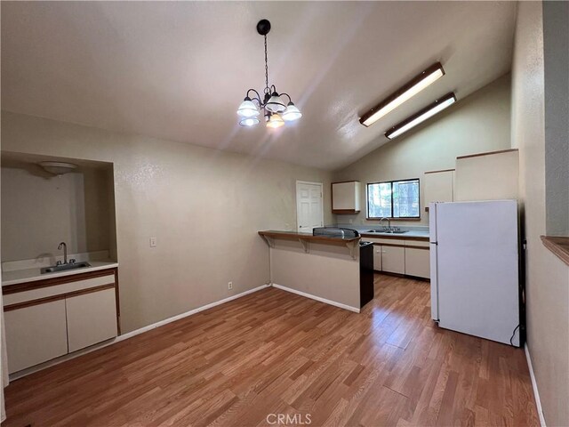 kitchen with a sink, white cabinets, freestanding refrigerator, light wood finished floors, and a chandelier