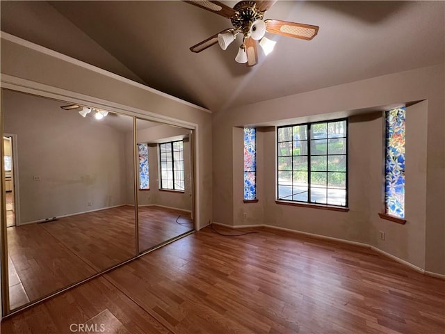 unfurnished bedroom with a closet, lofted ceiling, wood finished floors, baseboards, and a ceiling fan
