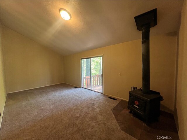 unfurnished living room with visible vents, a wood stove, baseboards, lofted ceiling, and carpet flooring