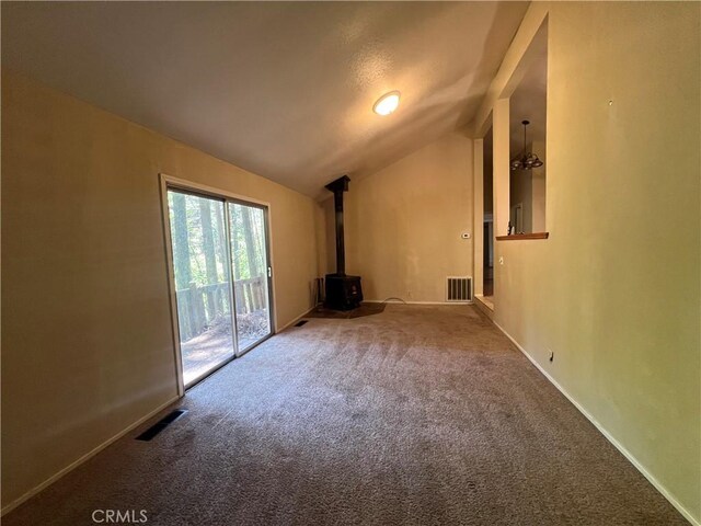 carpeted spare room featuring vaulted ceiling, baseboards, a wood stove, and visible vents