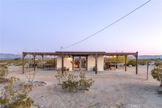 back of house at dusk with a patio, stucco siding, and french doors