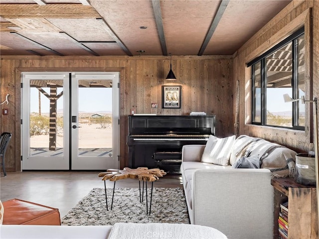 living room with plenty of natural light, finished concrete flooring, wooden walls, and french doors