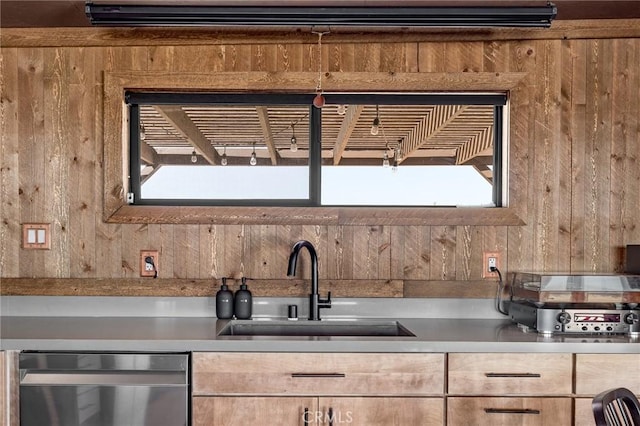 kitchen with a sink, dishwasher, wooden walls, and light countertops