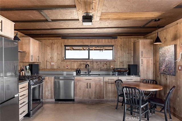kitchen with concrete flooring, appliances with stainless steel finishes, hanging light fixtures, a sink, and wood walls