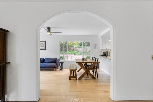 dining space featuring arched walkways, ceiling fan, and light wood-type flooring