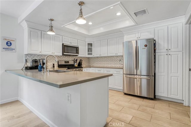 kitchen with decorative backsplash, a peninsula, white cabinets, a sink, and appliances with stainless steel finishes