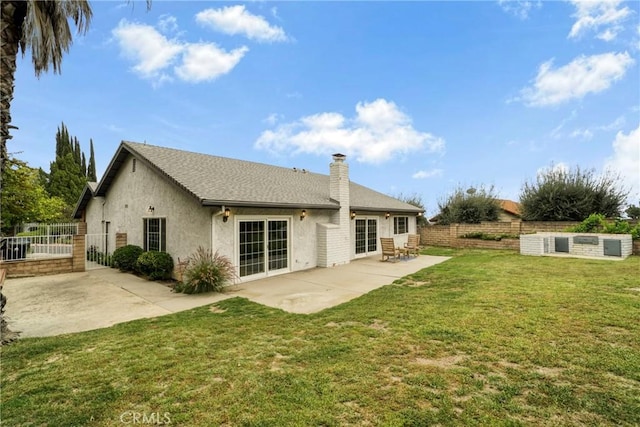 rear view of house with fence, stucco siding, a chimney, a patio area, and a lawn