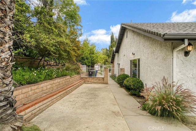 view of side of home with a gate, roof with shingles, stucco siding, and fence
