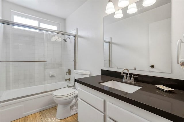 full bathroom with vanity, combined bath / shower with glass door, wood finished floors, and toilet