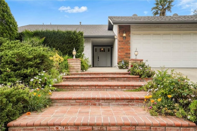 doorway to property with roof with shingles, an attached garage, and driveway
