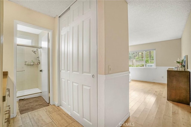corridor with a textured ceiling and light wood finished floors