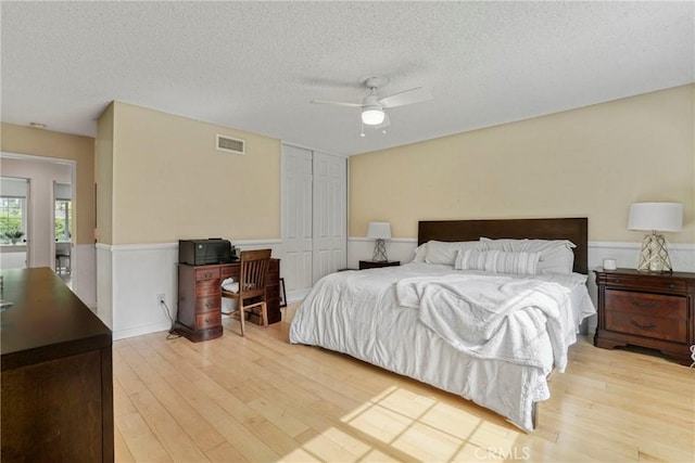 bedroom with visible vents, a closet, light wood-style floors, a textured ceiling, and a ceiling fan