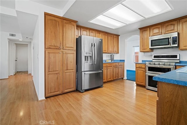 kitchen with brown cabinets, arched walkways, stainless steel appliances, light wood-type flooring, and visible vents
