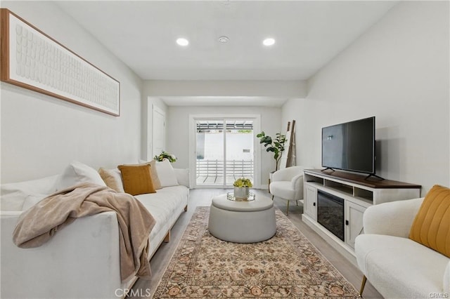 living area with recessed lighting, a glass covered fireplace, and light wood finished floors