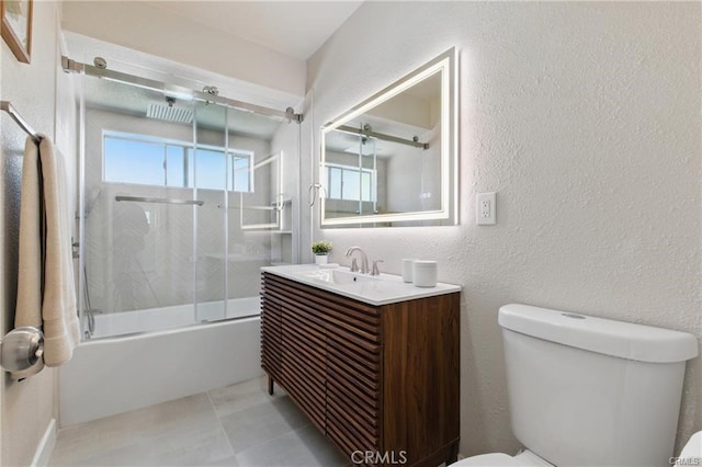 bathroom with vanity, a textured wall, combined bath / shower with glass door, and toilet