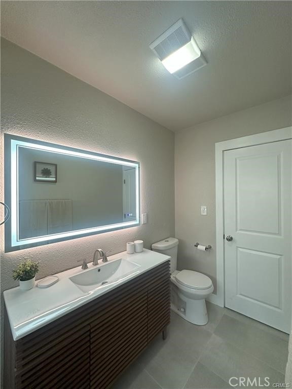 bathroom with toilet, a textured wall, visible vents, and vanity