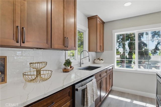 kitchen with backsplash, light stone countertops, dishwasher, a sink, and light wood-style floors