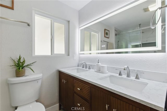 full bathroom with double vanity, toilet, a marble finish shower, and a sink