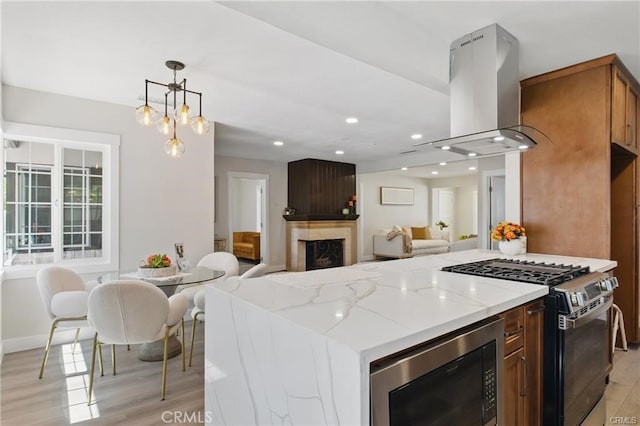 kitchen with island exhaust hood, built in microwave, light stone counters, and stainless steel gas range oven