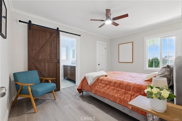 bedroom featuring light wood-style floors, crown molding, a barn door, and connected bathroom