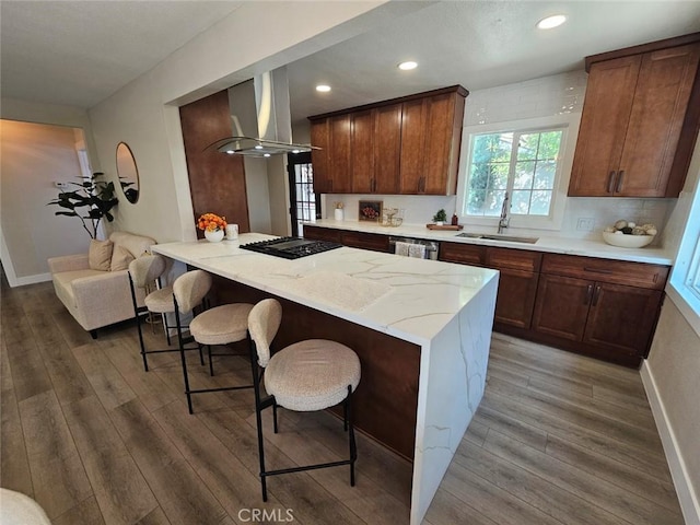kitchen with light stone countertops, a breakfast bar, a sink, wall chimney exhaust hood, and wood finished floors