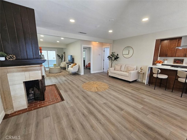 living area with visible vents, a fireplace, baseboards, light wood-style floors, and recessed lighting